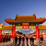 **Prompt:** A majestic, vibrant red Paeru Gate, the main entrance to Incheon Chinatown, adorned with intricate golden dragon motifs and Chinese characters. The gate stands prominently under a warm evening sky, with its grand architecture symbolizing the cultural harmony between Korea and China. People are seen in the foreground, admiring and taking photos, reflecting the lively atmosphere.